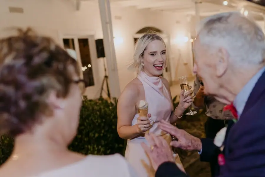 Bridesmaid laughing with older guests while holding an ice-cream cone