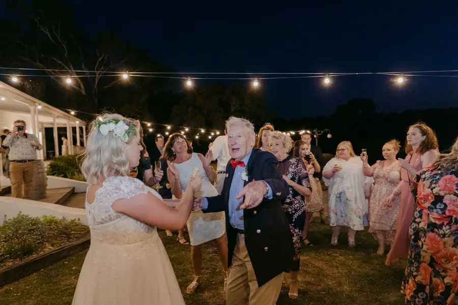 Bride and an older man dancing beneath outdoor lights