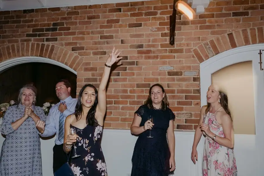 Guests dancing with drinks and raised hands in a brick-walled reception room