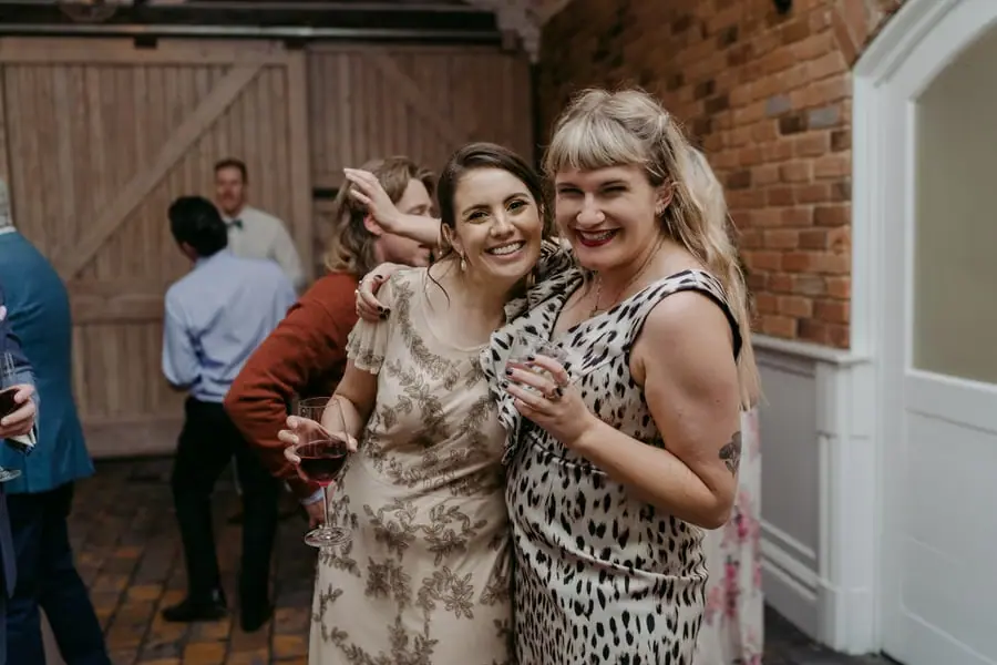 Two women leaning together and smiling with drinks indoors