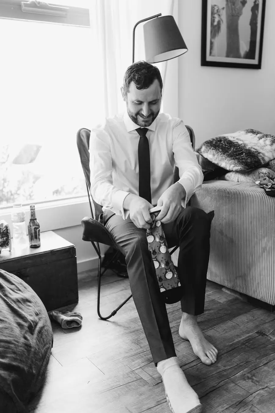 Black and white photograph of the groom putting on his shoes while seated