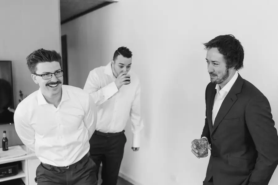 Black and white photograph of three men laughing together with drinks