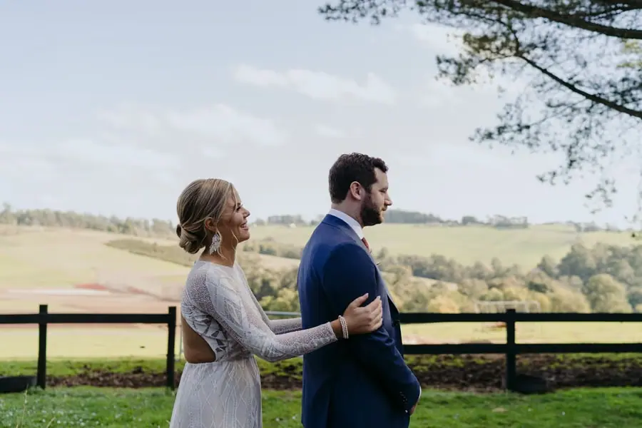 Bride resting her hand on the groom's shoulder beside a paddock fence