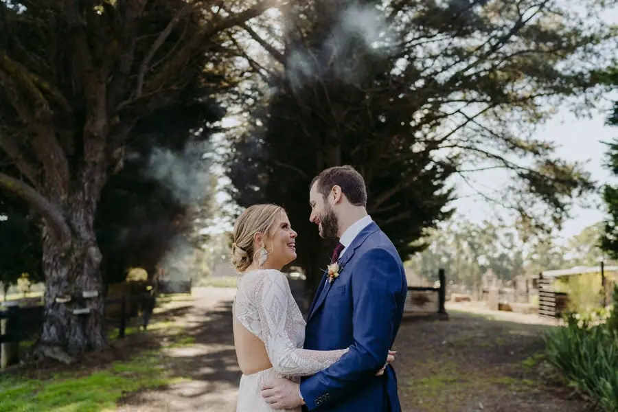 Bride and groom laughing together beneath tall trees
