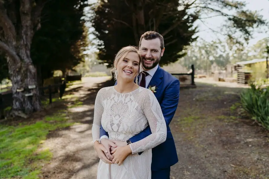 Groom embracing the smiling bride from behind on a country driveway