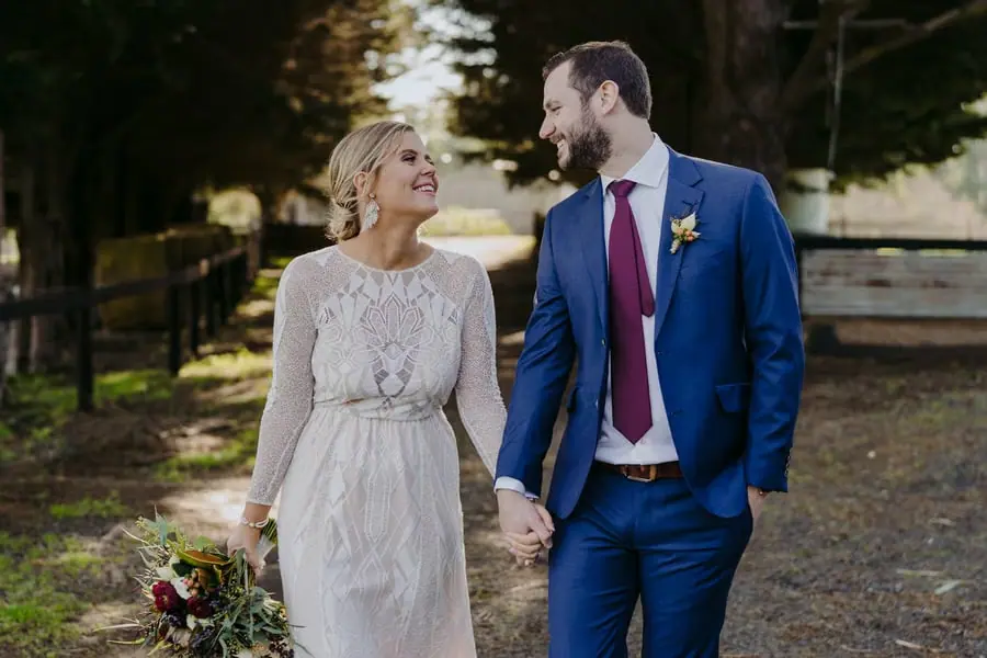 Bride and groom holding hands while walking beneath trees