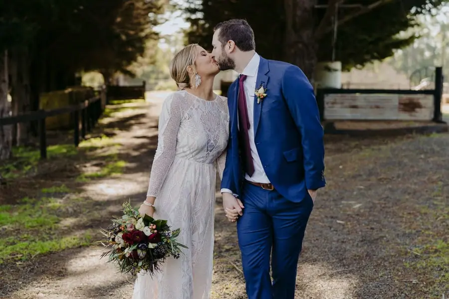 Bride and groom kissing while holding hands on a country driveway