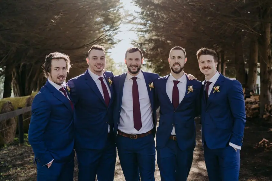 Groom and four groomsmen posing together in blue suits and burgundy ties