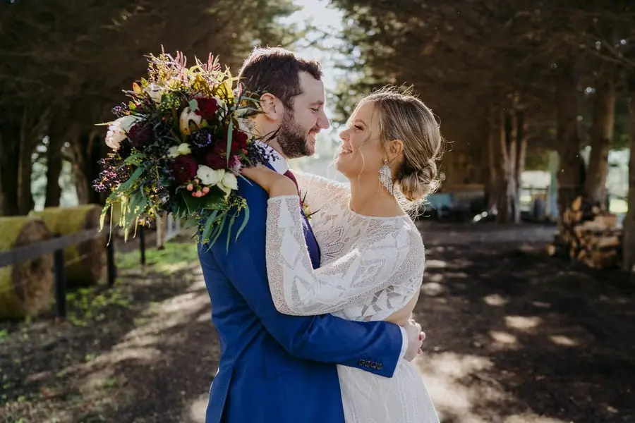 Bride and groom embracing with her bouquet resting near his shoulder