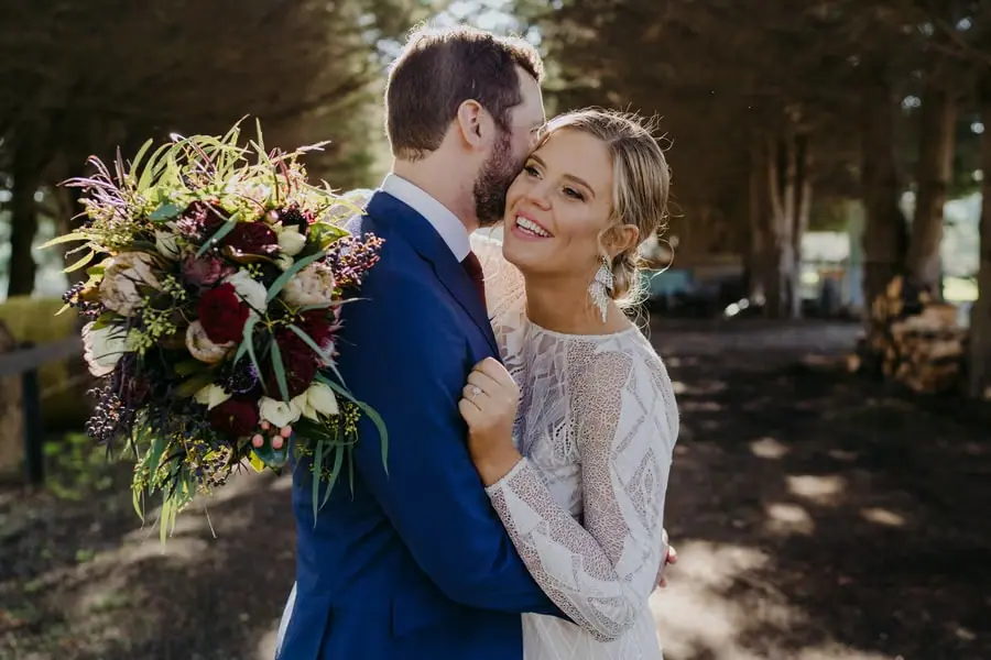 Groom kissing the bride's temple as she smiles in his arms