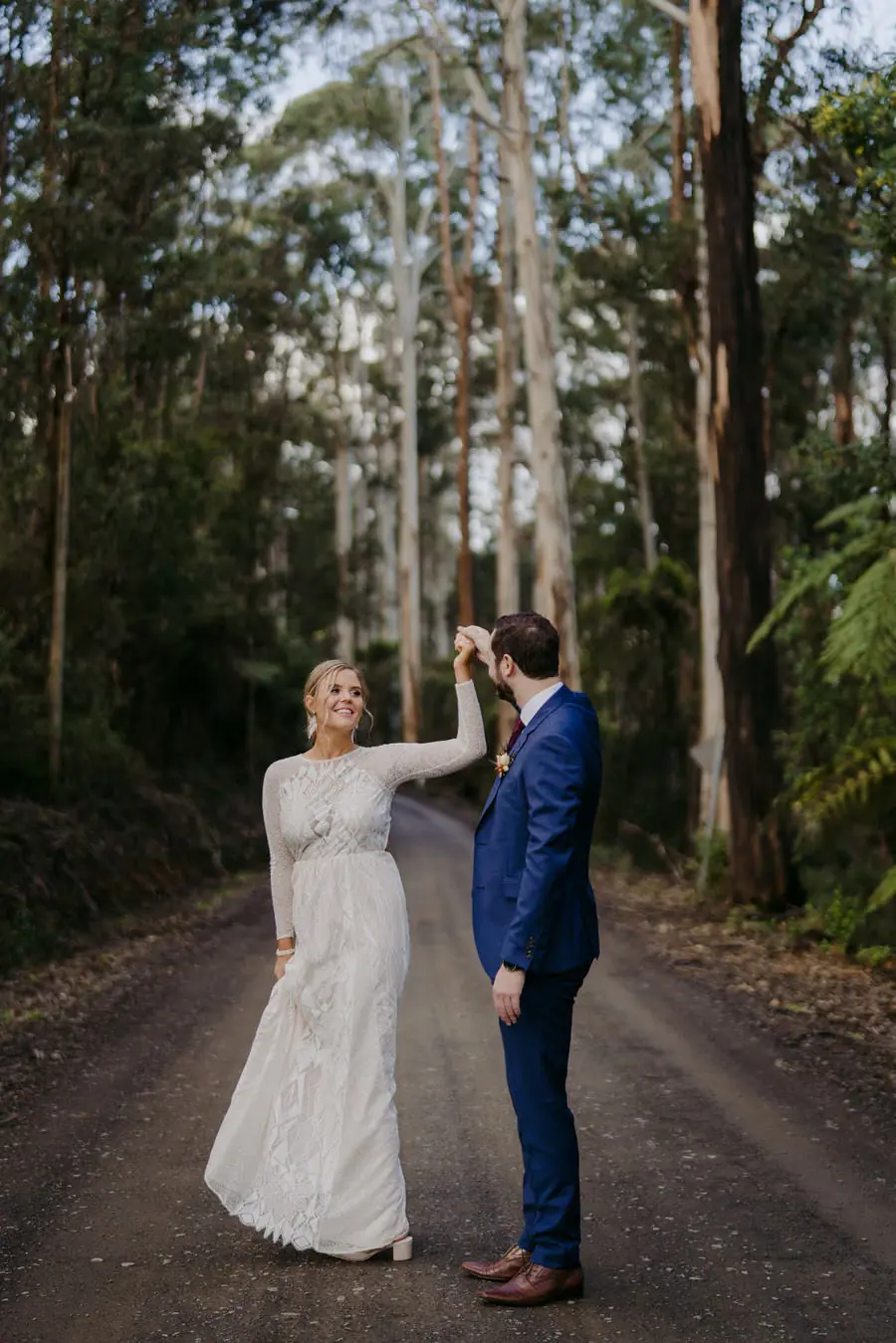 Groom holding the bride's hand above her head as she twirls on a forest road