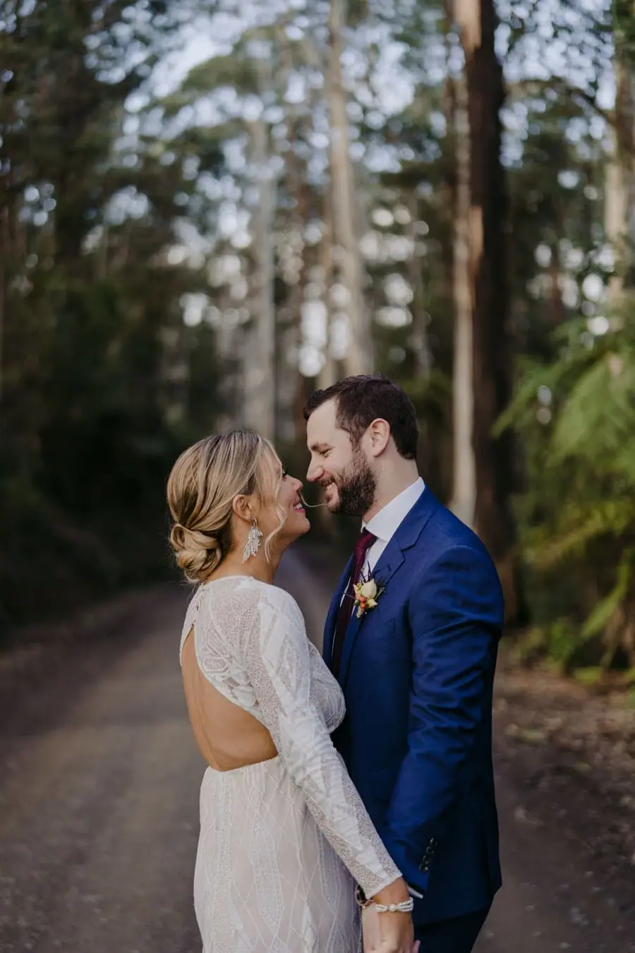 Bride and groom smiling at each other on a forest road