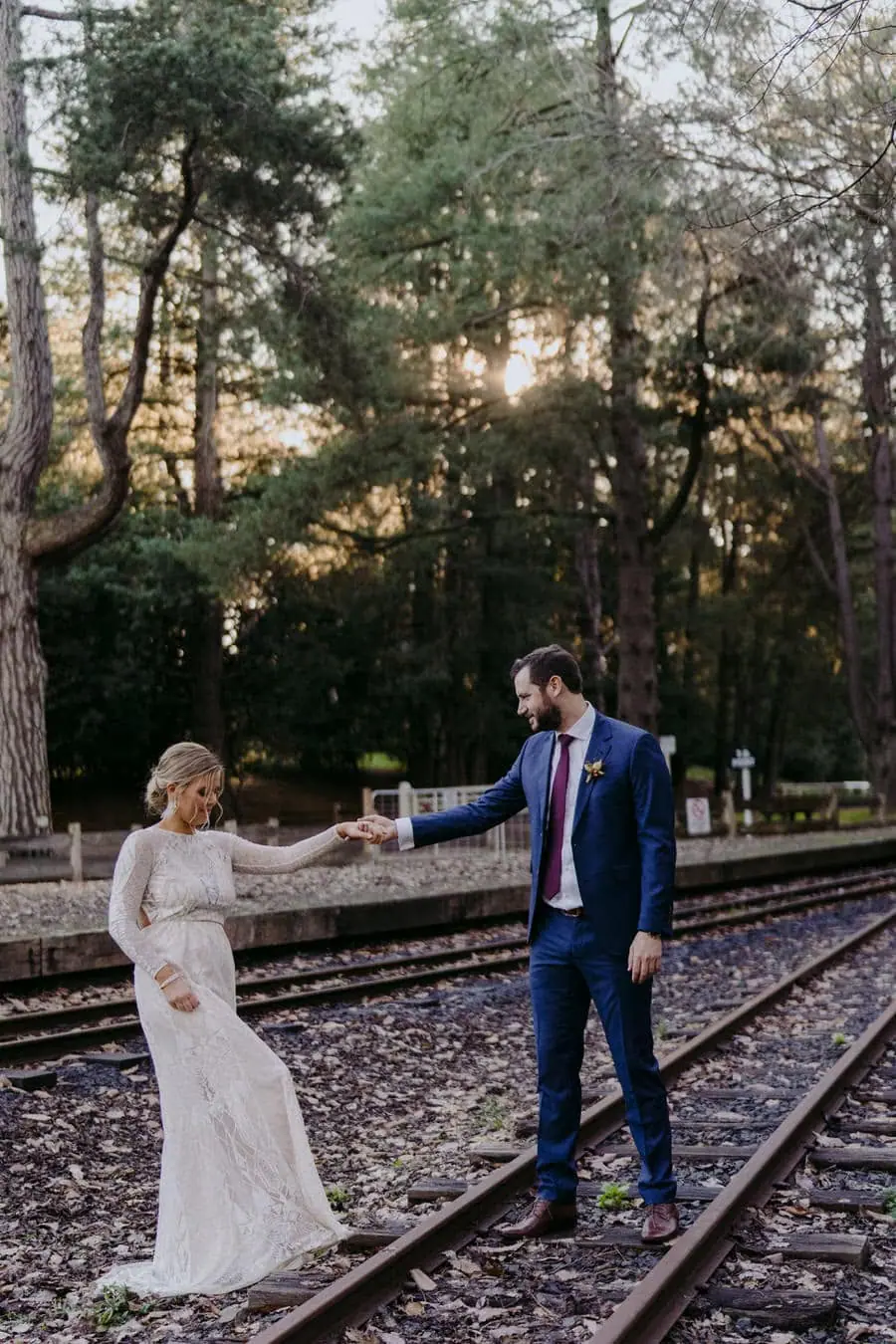 Bride and groom reaching toward each other while standing on railway tracks