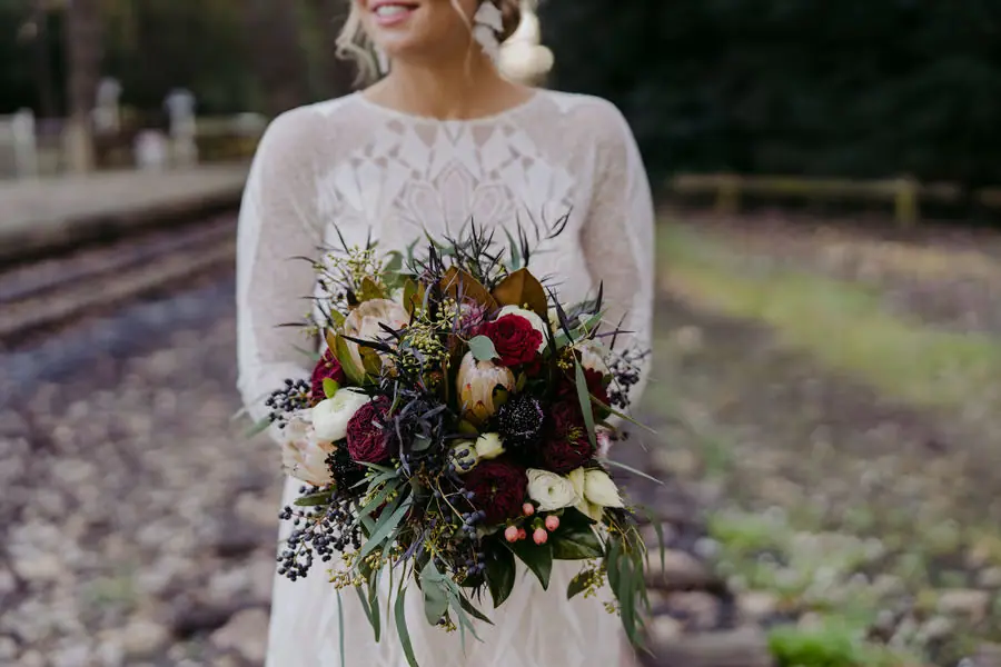 Bride holding a bouquet of burgundy and pale flowers with trailing greenery