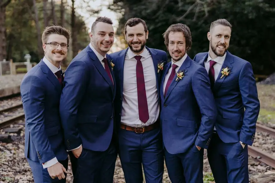 Groom and four groomsmen smiling together beside railway tracks