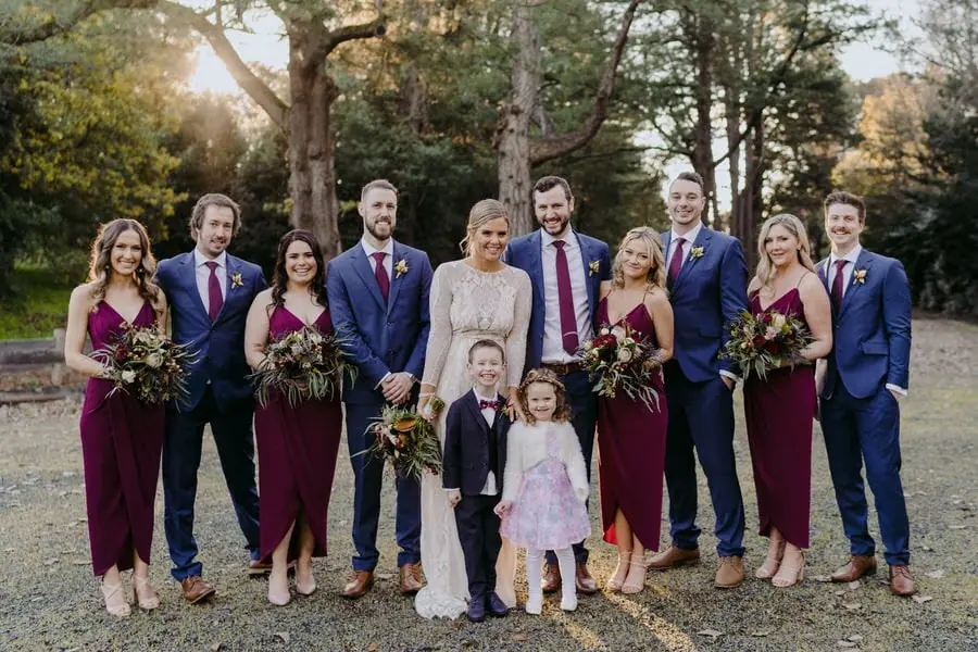 Wedding party posing together with two children beneath trees