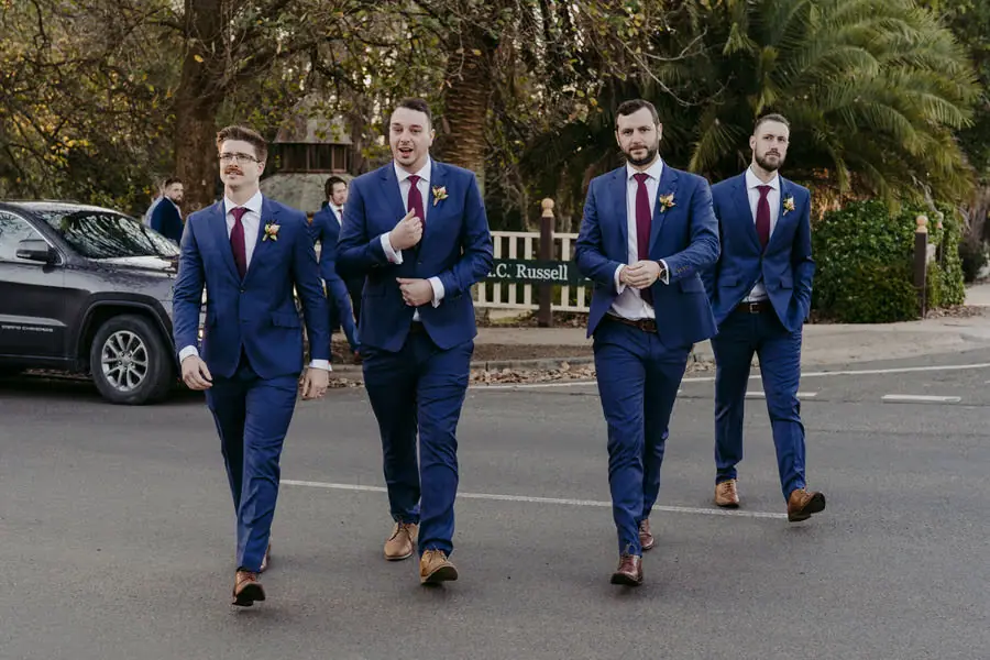 Groomsmen in blue suits crossing a street outside the wedding venue