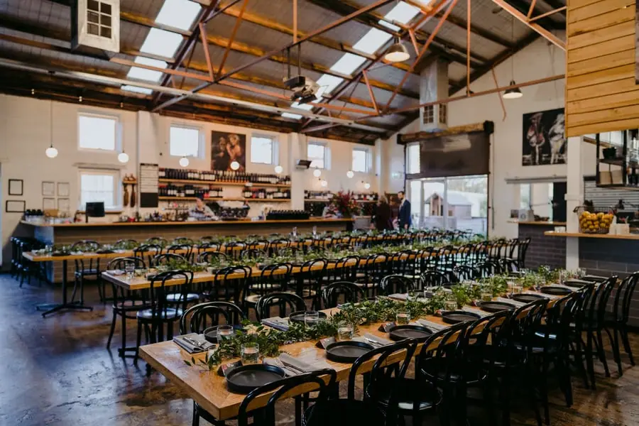 Long reception tables set with black plates and greenery beneath exposed roof beams