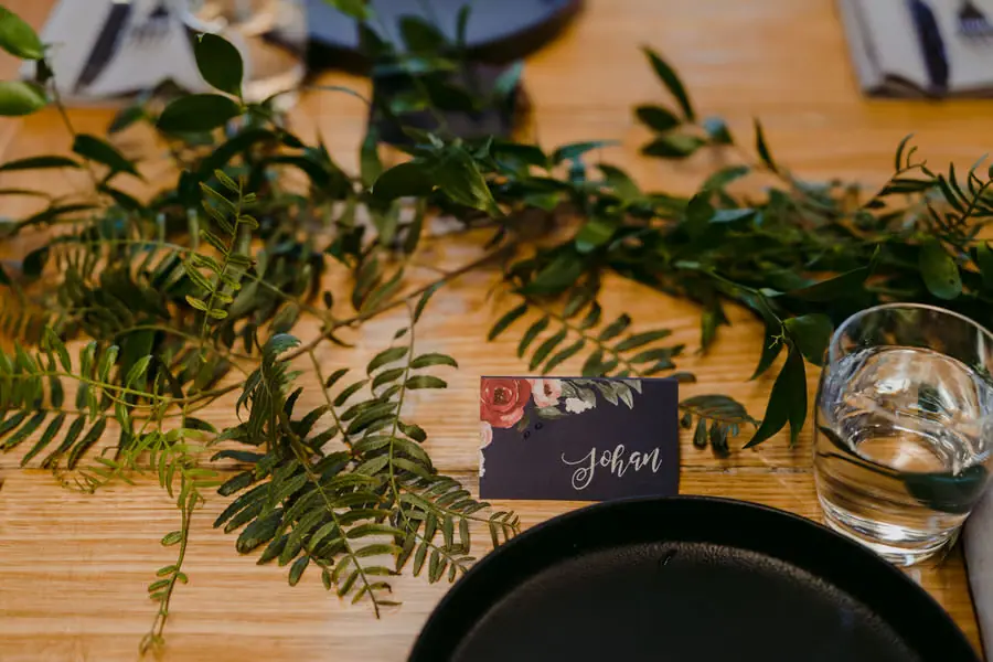 Place card beside greenery, a black plate and a water glass