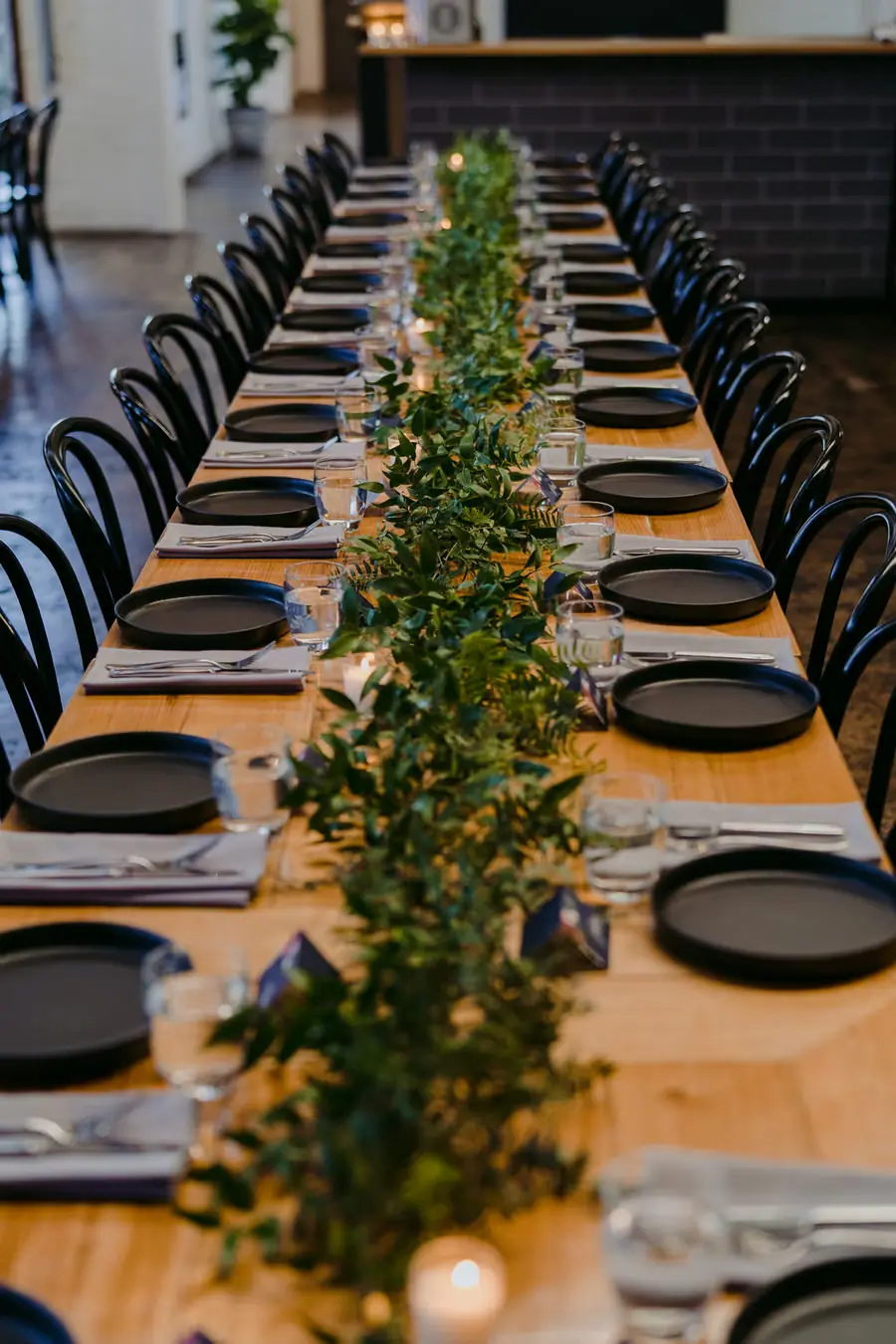 Long wooden reception table decorated with greenery and black place settings