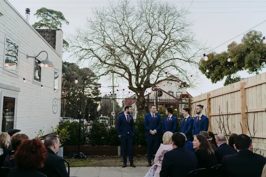Groom and groomsmen waiting before seated guests in an outdoor courtyard