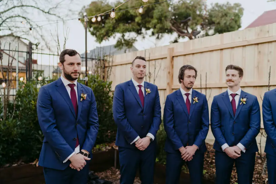 Groom and groomsmen standing in blue suits and burgundy ties