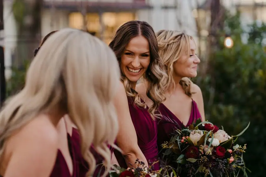 Bridesmaids smiling together while holding dark red and pale bouquets