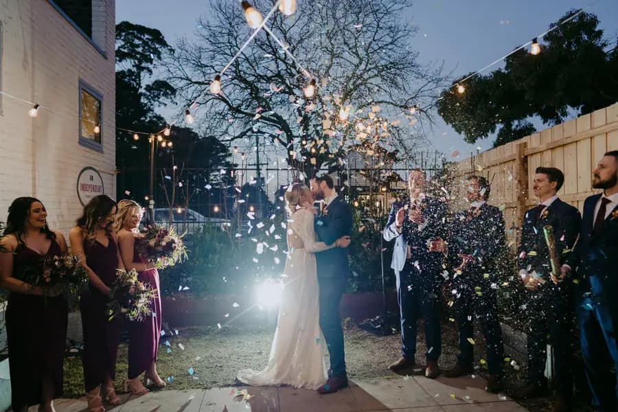 Bride and groom embracing beneath falling confetti in the courtyard