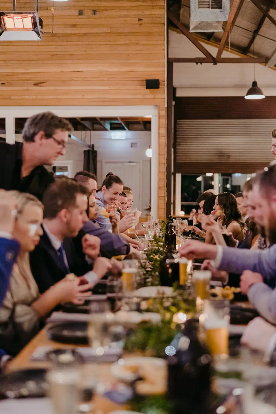 Guests eating and chatting along a long wooden reception table
