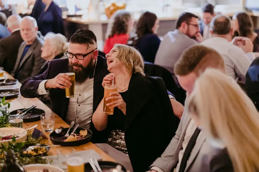 Two seated guests smiling together over drinks at the reception