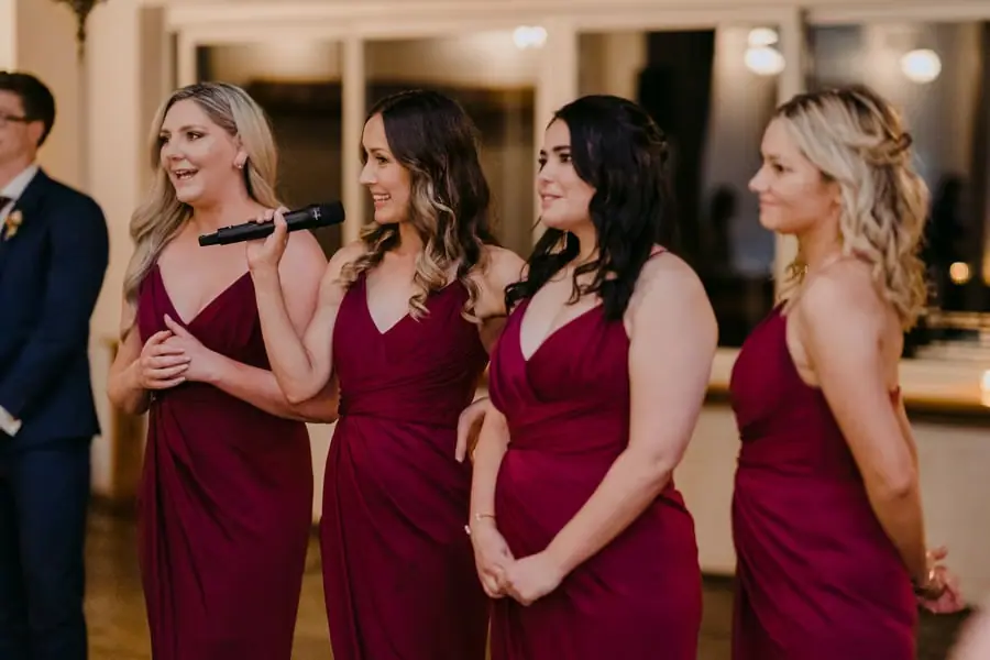 Four bridesmaids in burgundy dresses smiling together during reception speeches