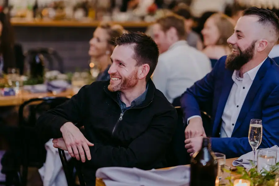 Two men laughing while seated together at a reception table