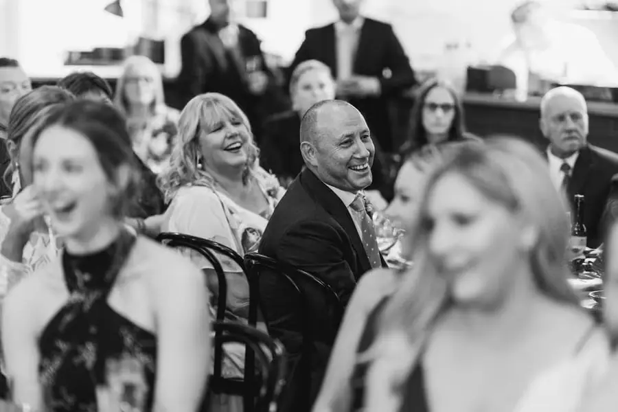 Black and white photograph of seated guests laughing during the reception