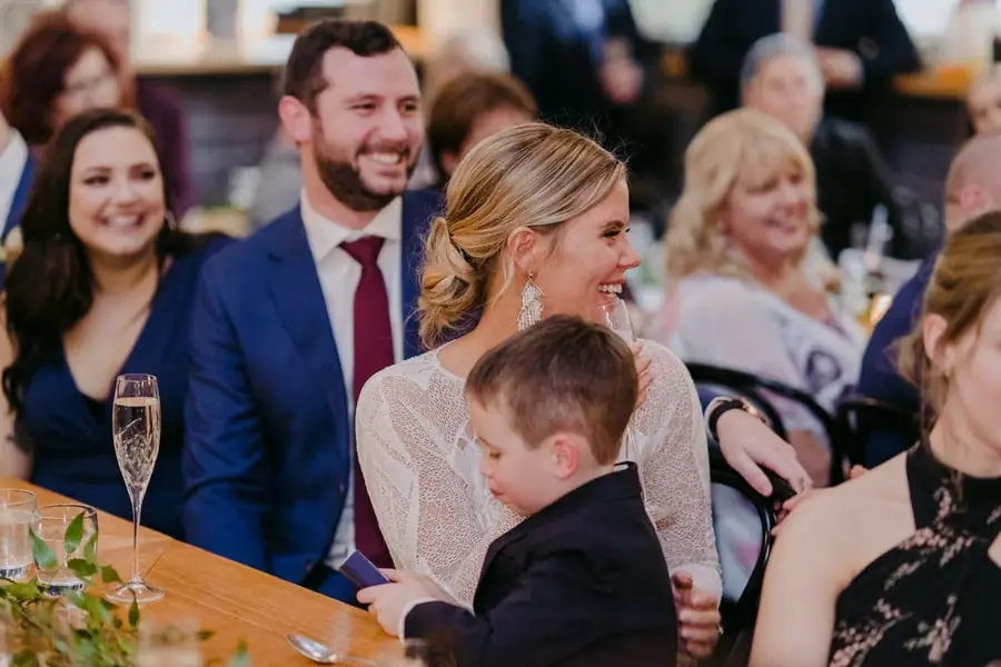 Bride and groom smiling at the reception table with a young boy beside them