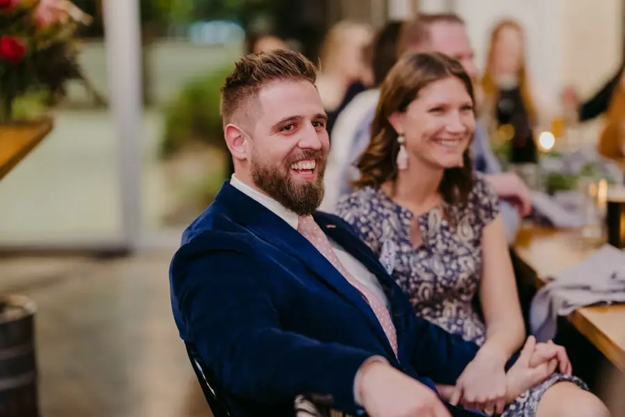 Guest in a blue velvet jacket smiling while seated at the reception