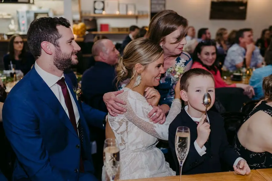 Woman embracing the seated bride as the groom and a young boy watch