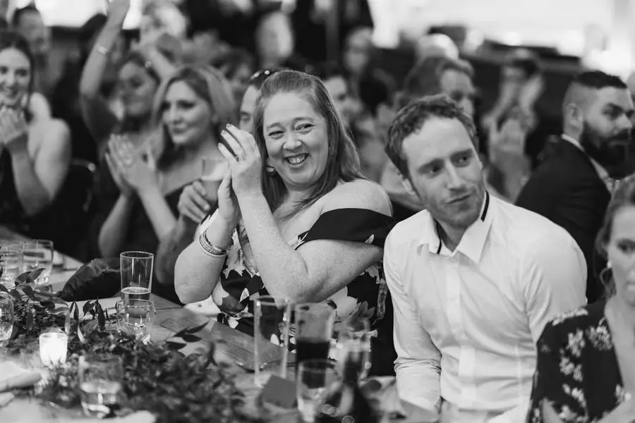 Black and white photograph of a smiling guest applauding at the reception table