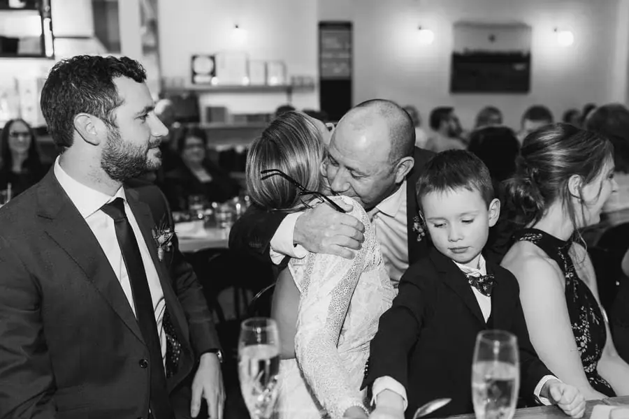 Black and white photograph of a guest hugging the bride beside the groom and children