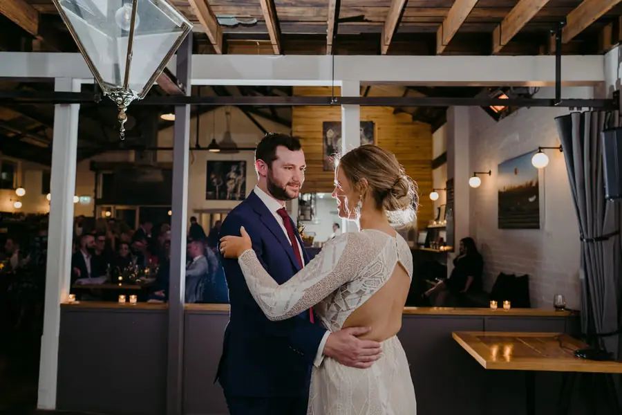 Bride and groom dancing together beneath exposed reception roof beams