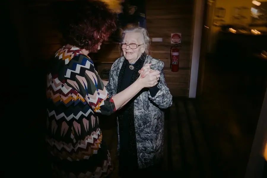Two women dancing hand in hand beneath warm reception lights