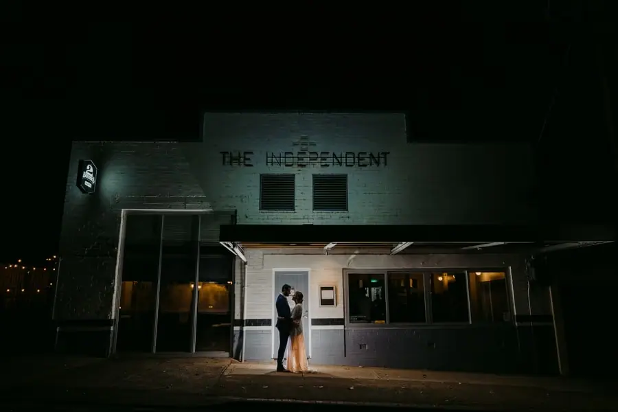 Bride and groom embracing in an illuminated doorway beneath The Independent sign at night