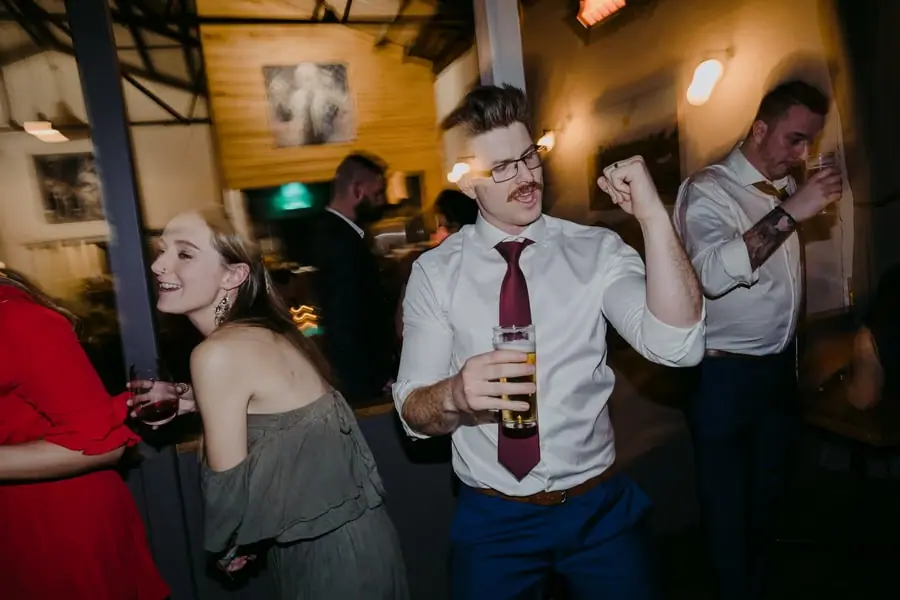 Guest with glasses holding a drink and raising his fist on the dance floor