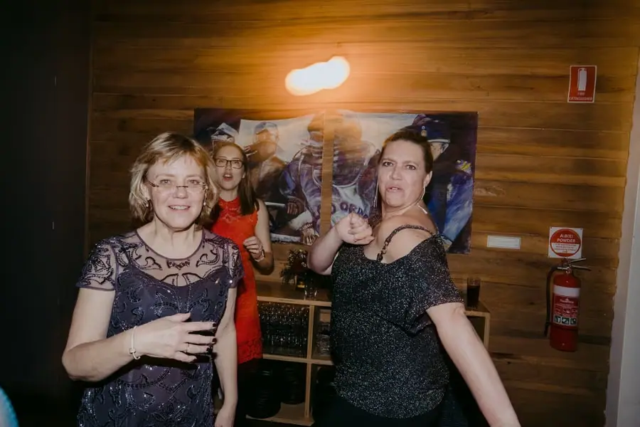 Two guests smiling with drinks beside a timber reception wall