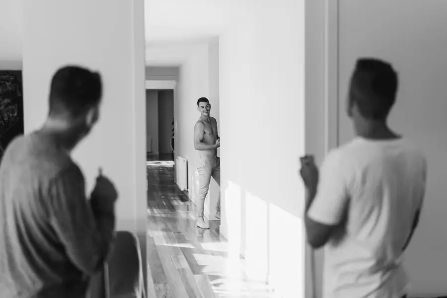 Black-and-white photograph of men getting ready in a sunlit hallway