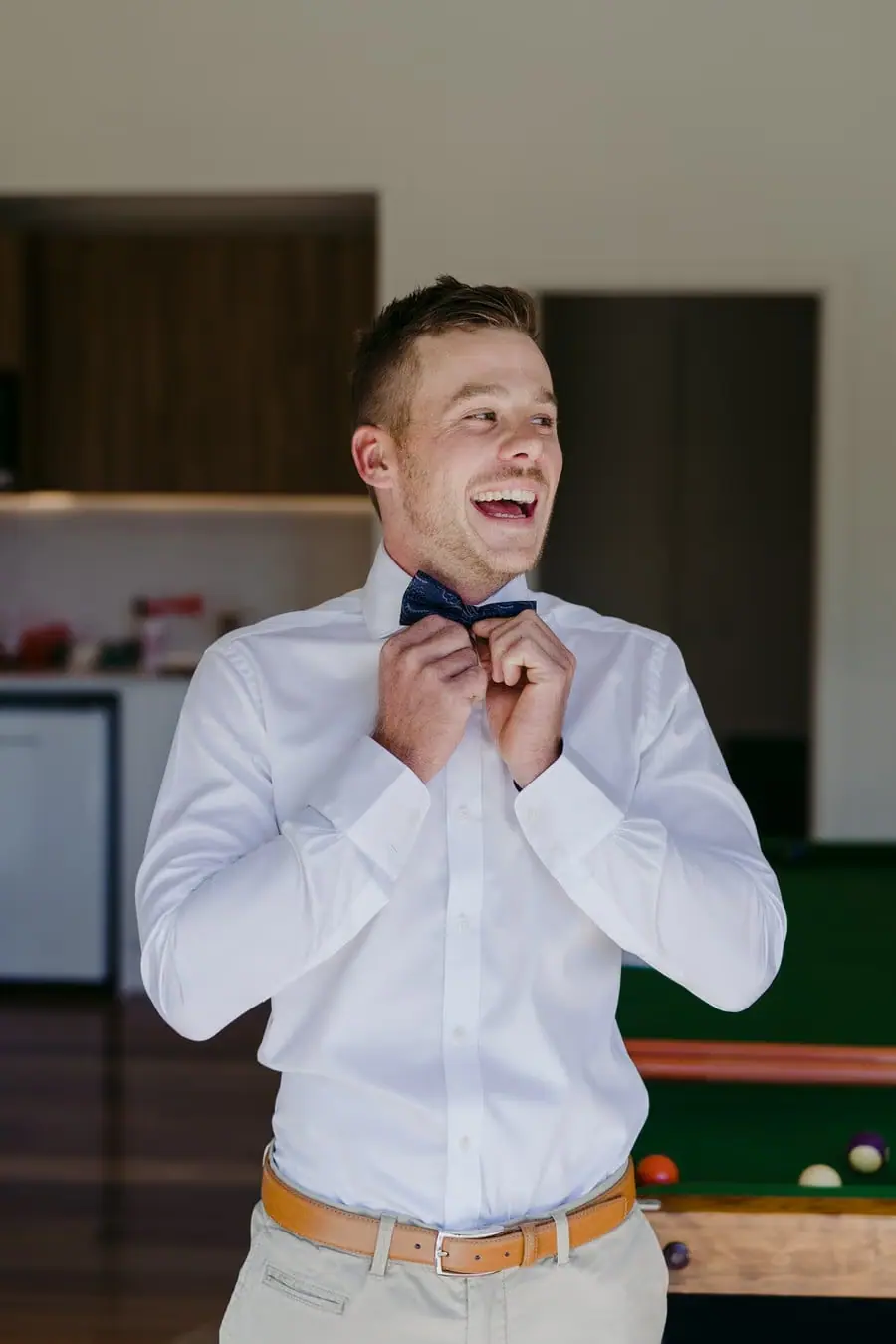 Groom laughing while adjusting his bow tie