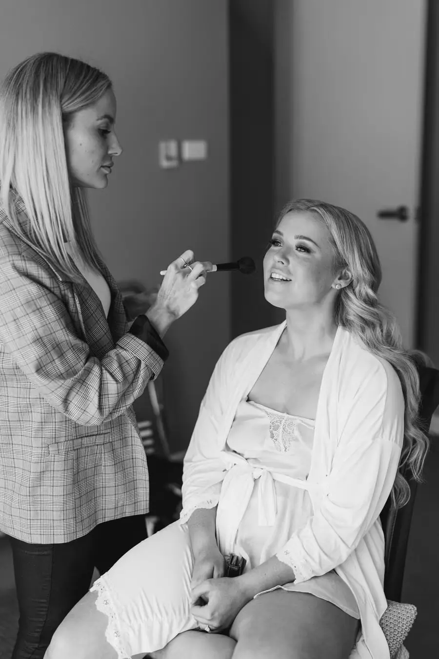 Black-and-white photograph of a makeup artist preparing the bride