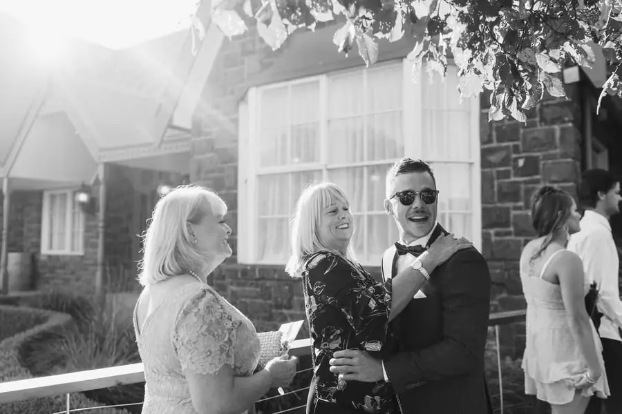 Black-and-white photograph of guests greeting each other outside a stone building