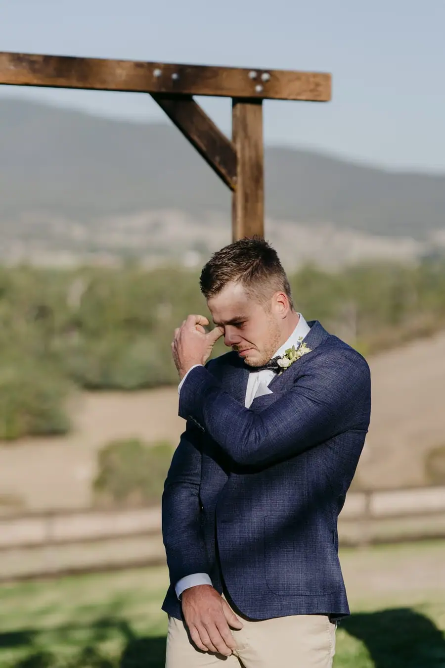 Groom wiping his eye while standing beneath the ceremony arch