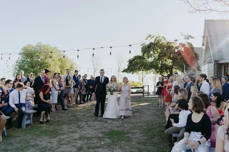 Bride walking beside an older man between rows of seated guests