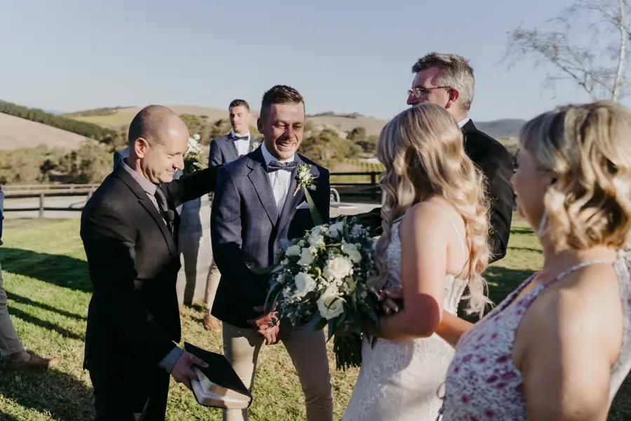 Bride and groom standing with a celebrant during the outdoor ceremony